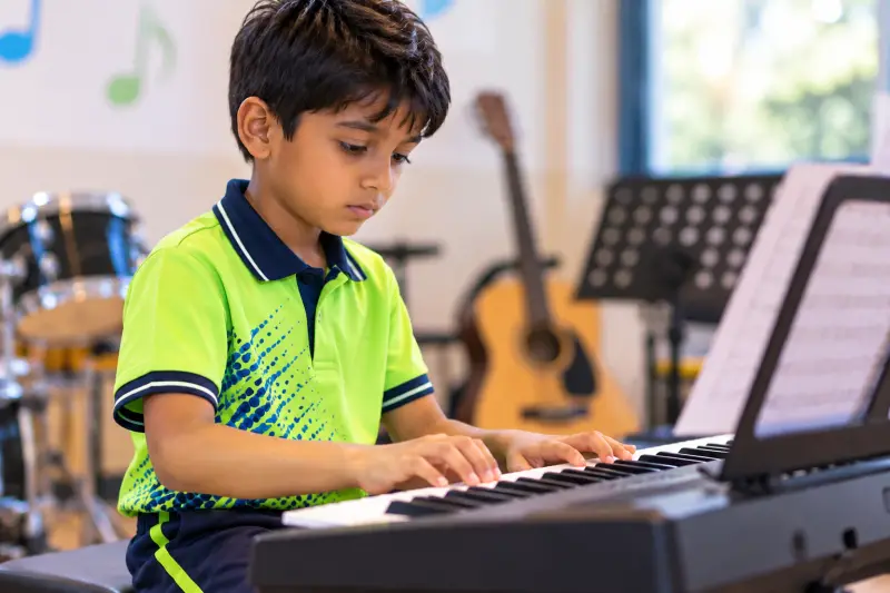 A student in the Sloka music room playing the keyboard, with a guitar and drums behind him.